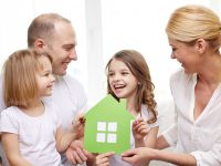 family, children, accommodation and home concept - smiling parents and two little girls at home with green house symbol